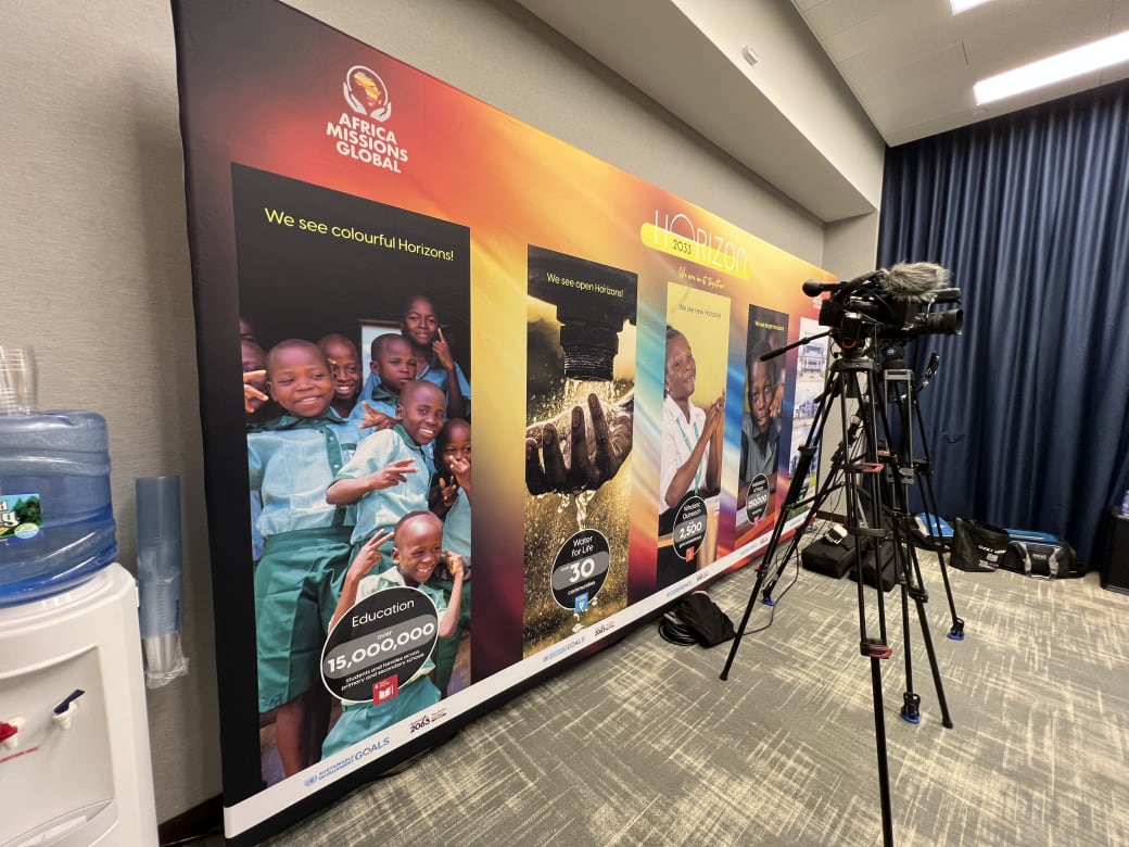 Horizon 2033 media wall with full-color photo panels and impact stats, with a press camera set up in front