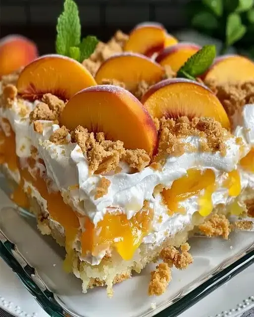 A slice of Heavenly Summer Peach Cobbler Poke Cake on a plate, showing layers of cake, pudding, and peach filling with whipped cream topping.