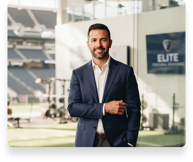 Coach in a blazer standing in a stadium with an Elite Personal Branding sign in the background