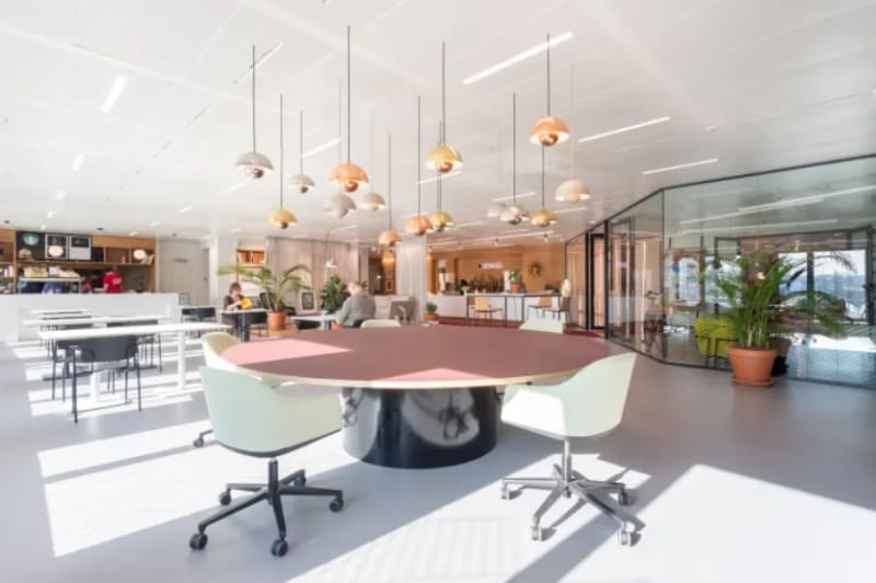 Zona de coworking abierta con mesa comunitaria y lámparas colgantes en Ciudad Lineal, Madrid