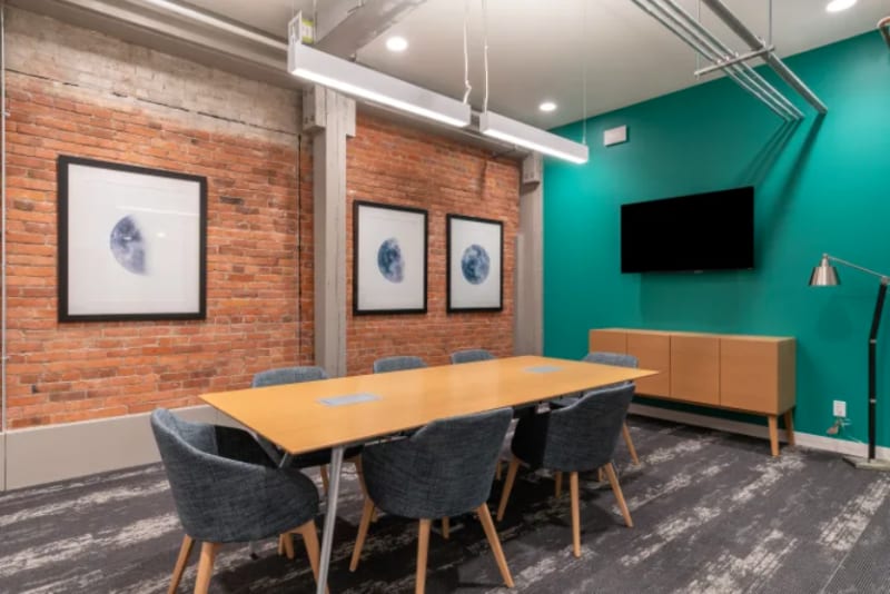 Sala de reuniones con pared de ladrillo visto, pantalla y mobiliario moderno en Ciudad Lineal, Madrid