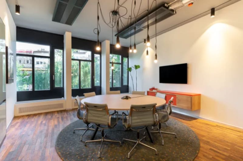 Sala de reuniones con mesa redonda y grandes ventanales con vistas a la vegetación en Ciudad Lineal, Madrid