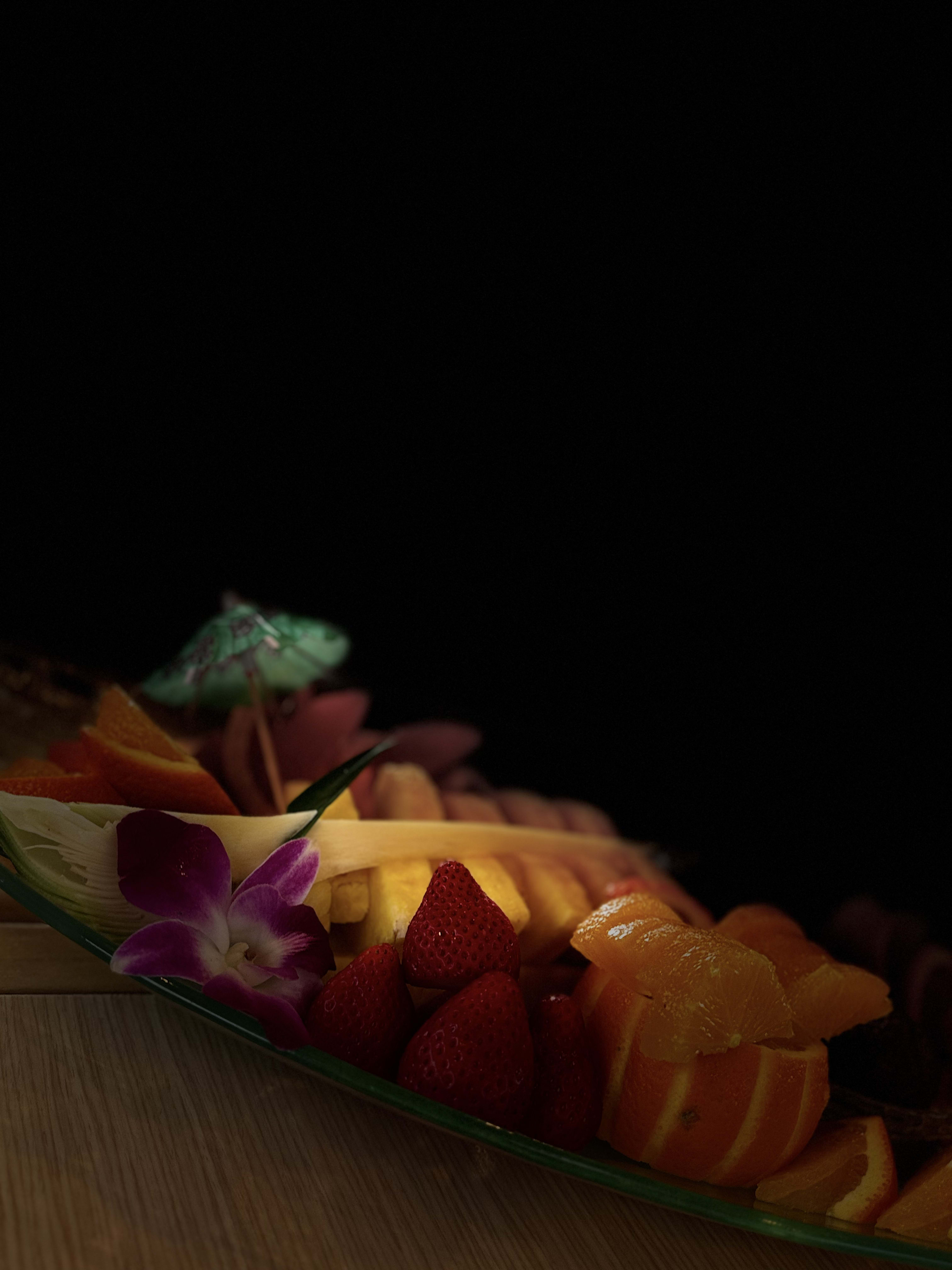 Close-up of strawberries and orange slices garnished with purple orchid flowers on a fruit platter
