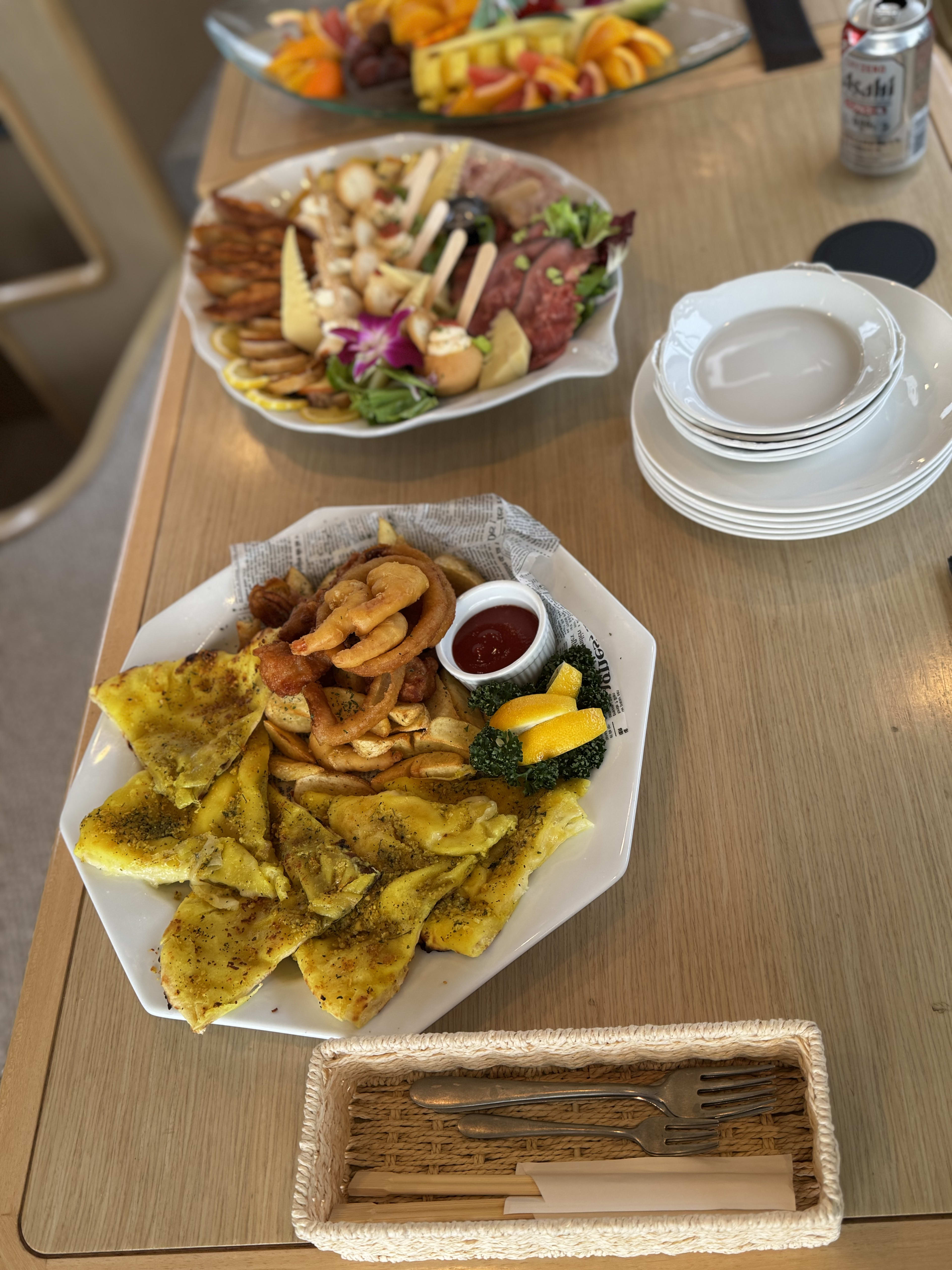 Seasoned potato wedges, a meat and cheese platter, plates and drinks set out for a meal on board