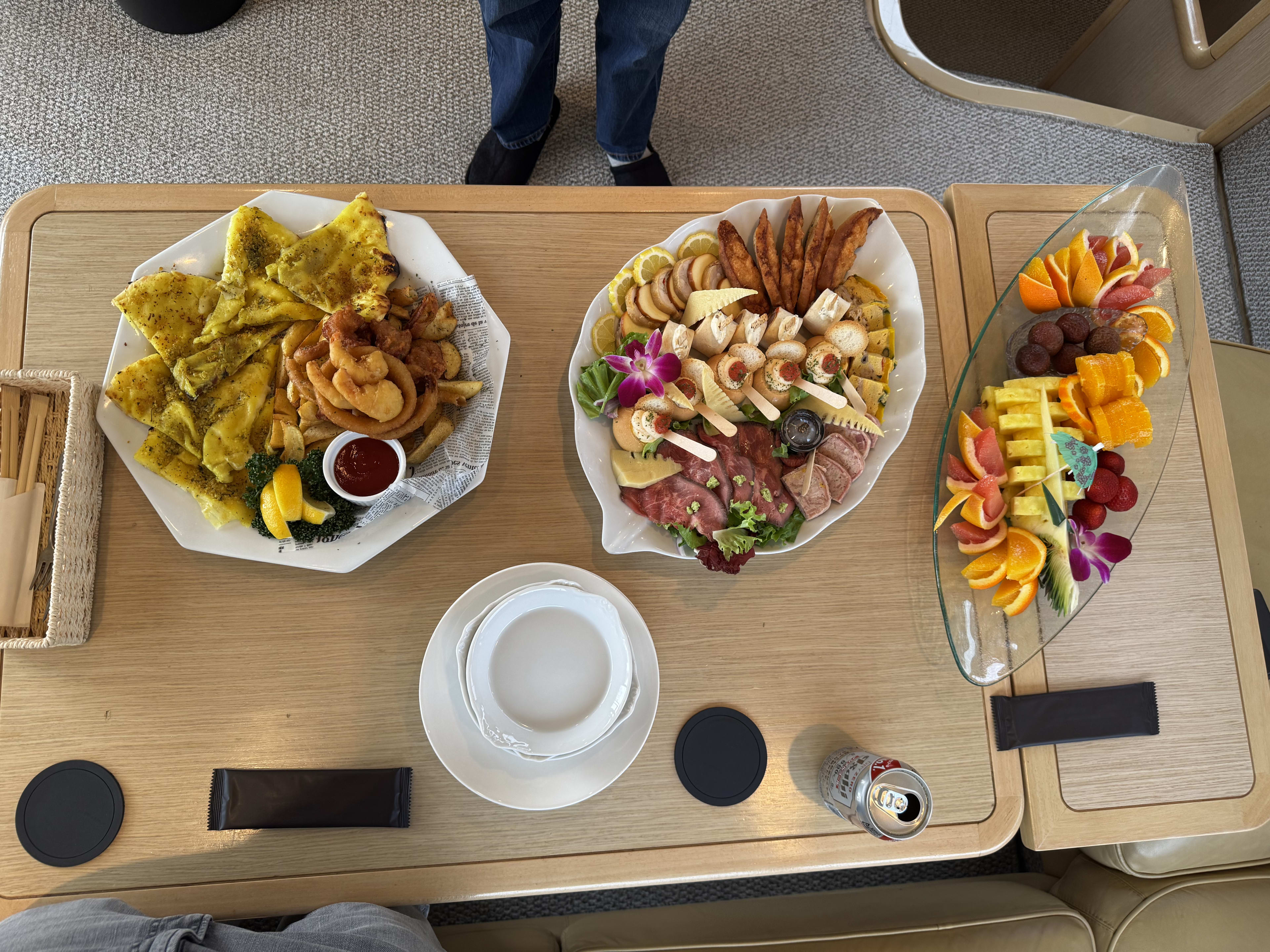 Three plates of appetizers beside a charcuterie board and fruit platter on a wooden table with drinks