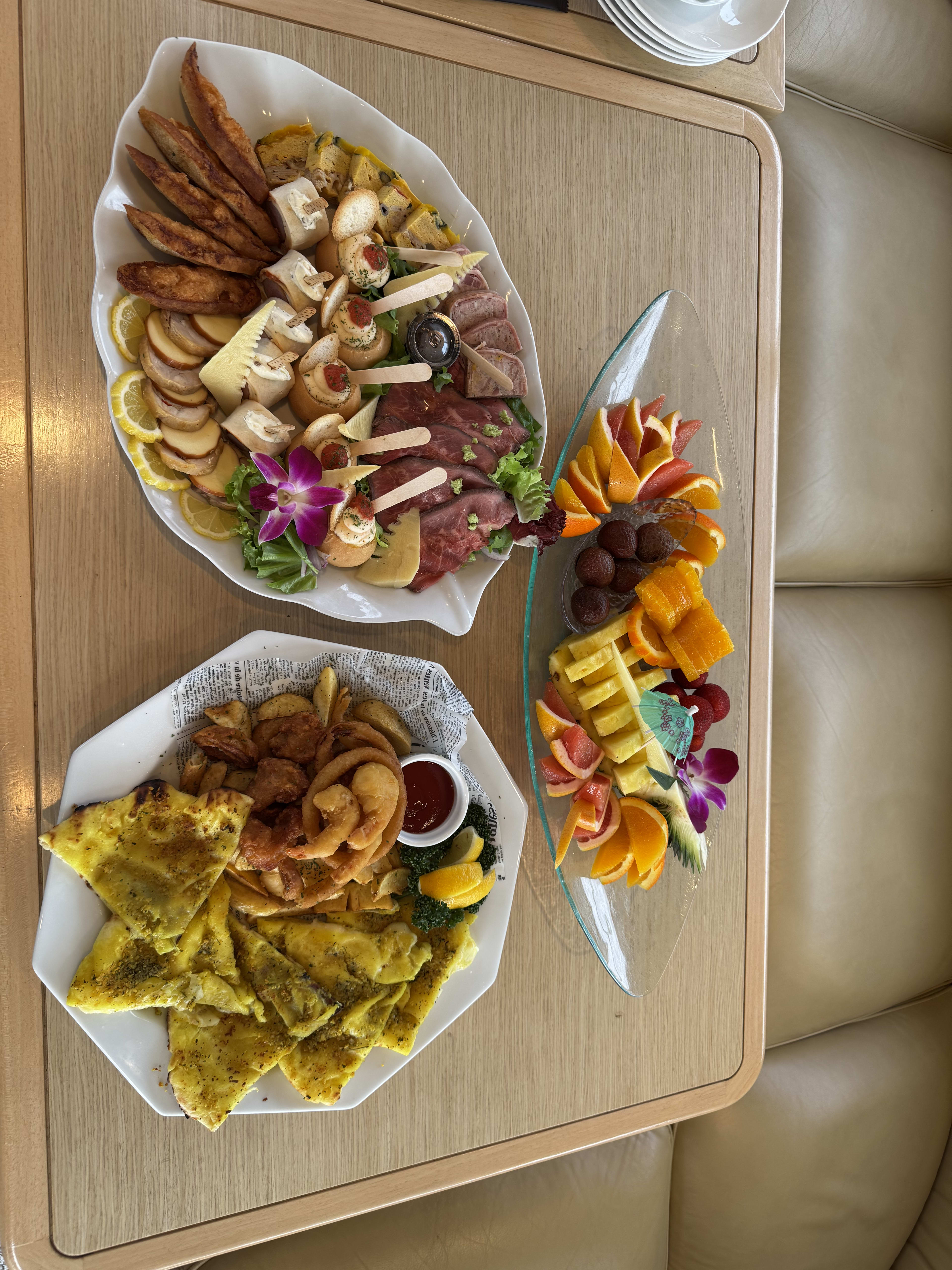 Charcuterie, flatbread with onion rings and a fruit platter with chocolates served with drinks on board