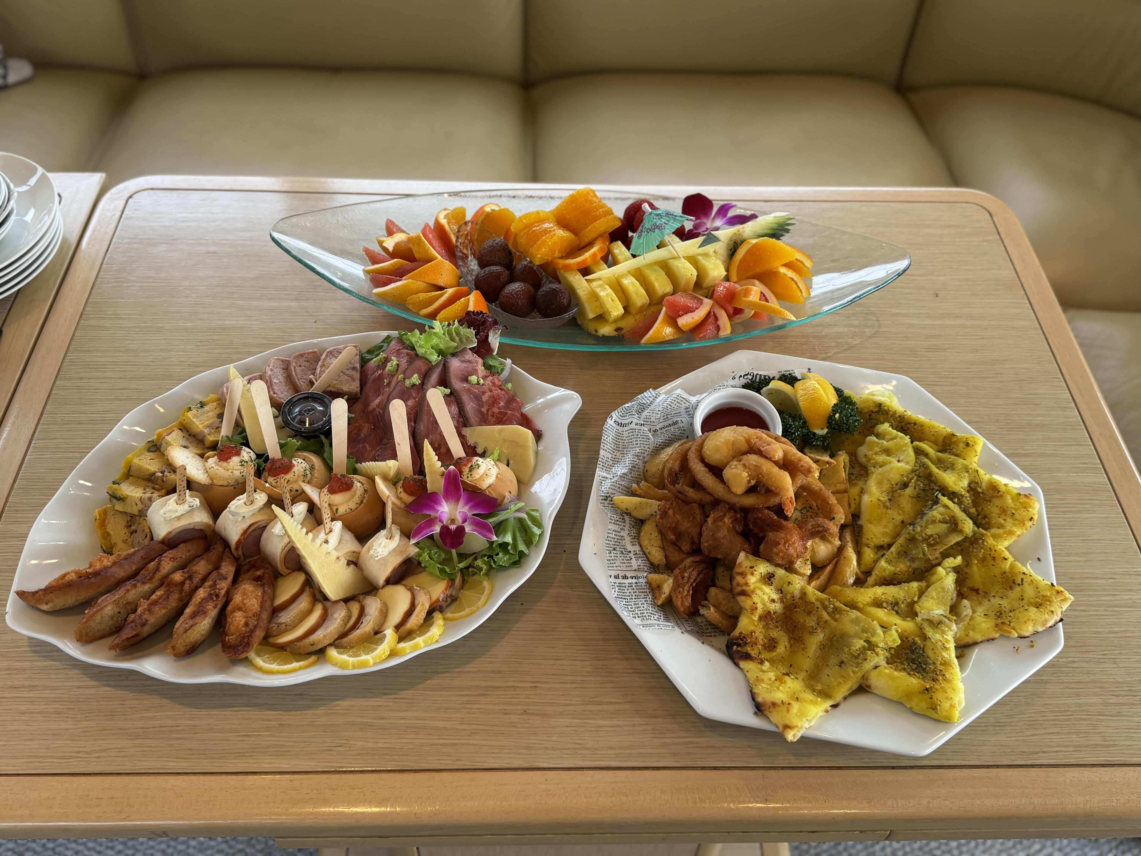 Fruit platter, charcuterie board with meats and cheeses, and an appetizer platter laid out on board