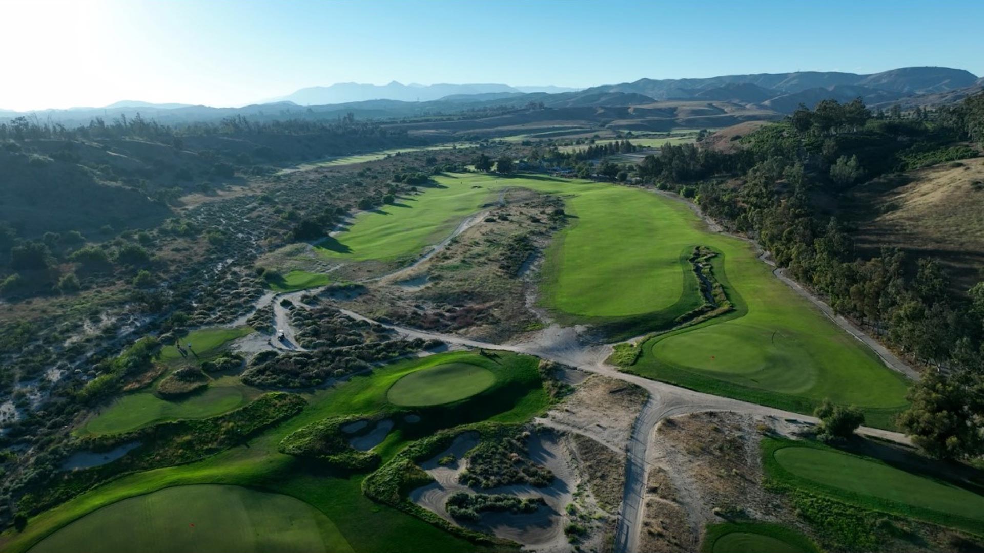 Breathtaking aerial perspective of the golf course nestled in rolling hills with layered mountain ranges extending to the horizon.