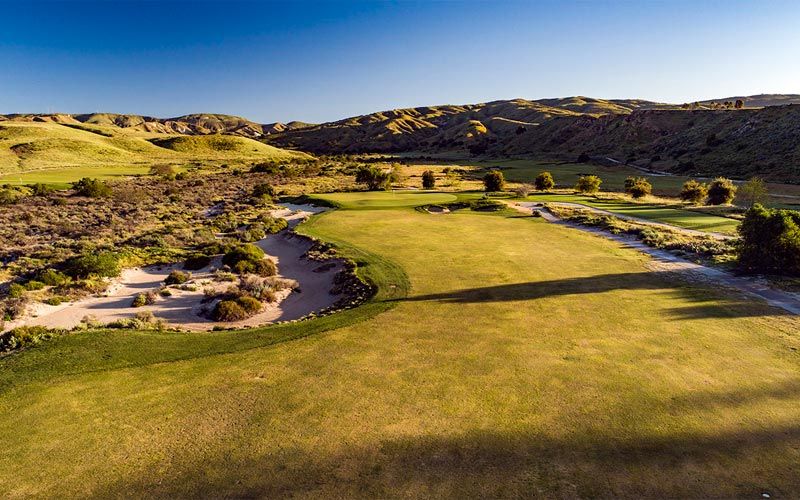Stunning aerial view of desert golf course with golden hour lighting showcasing rolling hills, green fairways, and natural desert landscape.