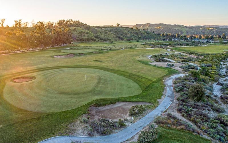 Elevated aerial view of a well-manicured putting green surrounded by desert vegetation and cart paths during golden hour.