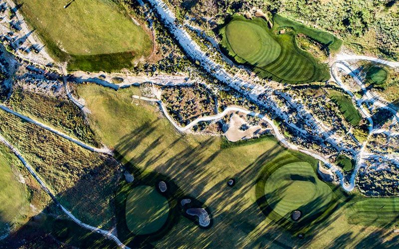 High-altitude aerial shot showing the complete golf course layout with multiple holes, cart paths, and shadows creating dramatic contrast.