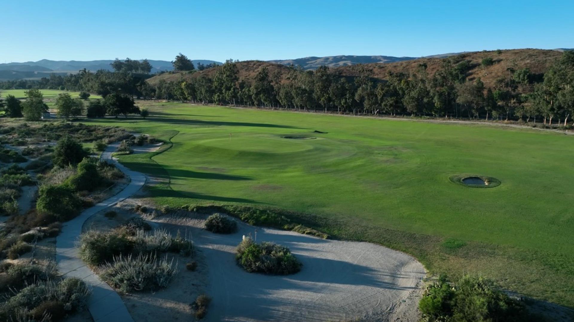 Ground-level view of a pristine fairway with artistic bunker design, framed by natural desert vegetation and distant mountains.