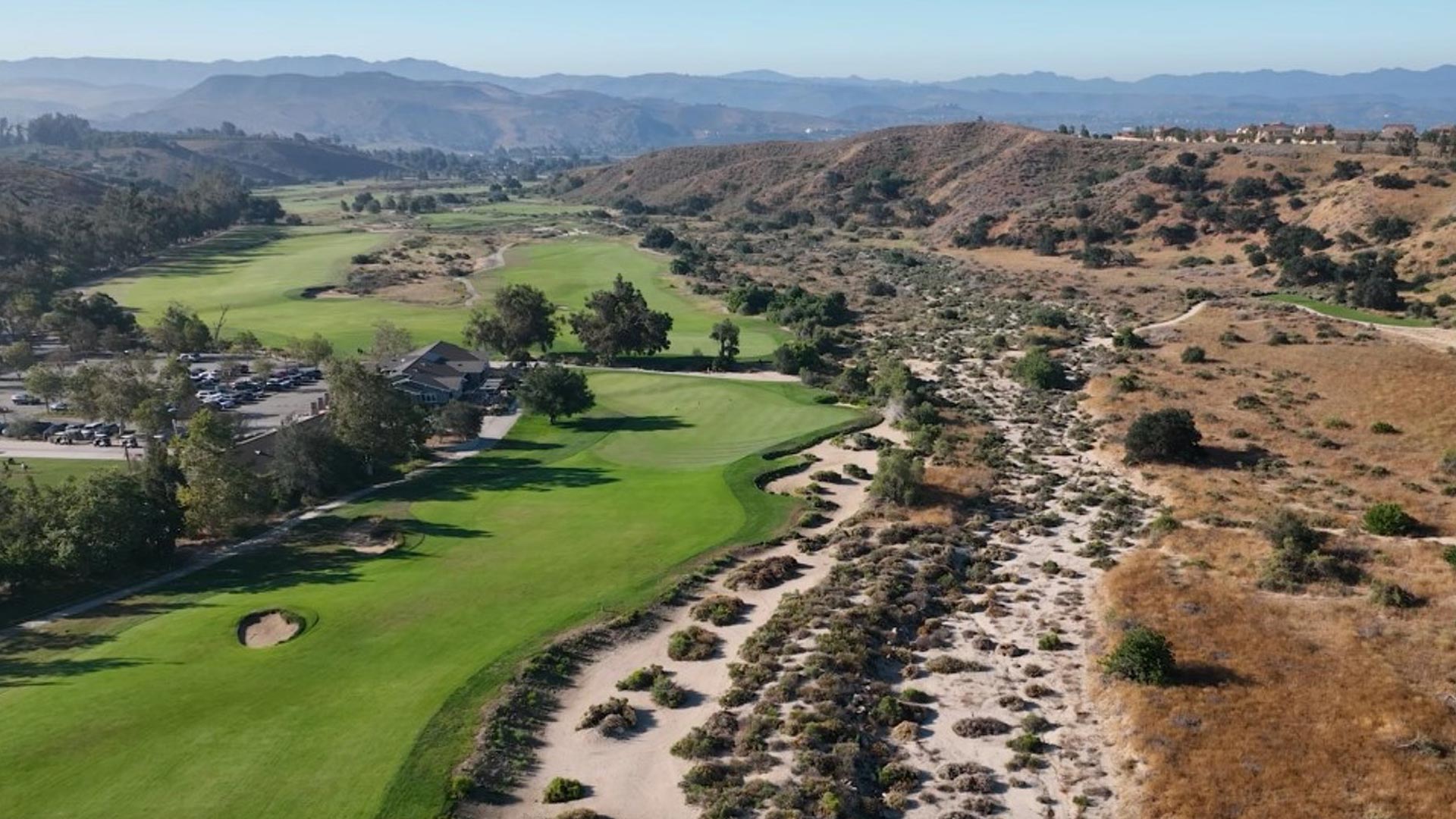 Elevated aerial view showing multiple holes and the clubhouse complex set against dramatic hillside terrain and desert landscape.