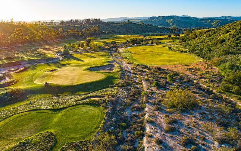 Sweeping aerial perspective of multiple golf holes with fairways, greens, and cart paths winding through desert terrain in warm lighting.