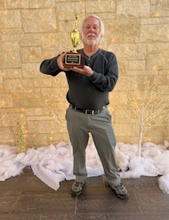 Male golfer holding a trophy award while standing against a stone wall background.