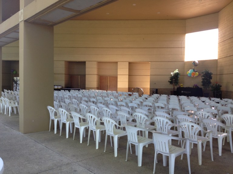An empty event pavilion with rows of white plastic chairs set up for a ceremony or presentation under a modern covered structure.