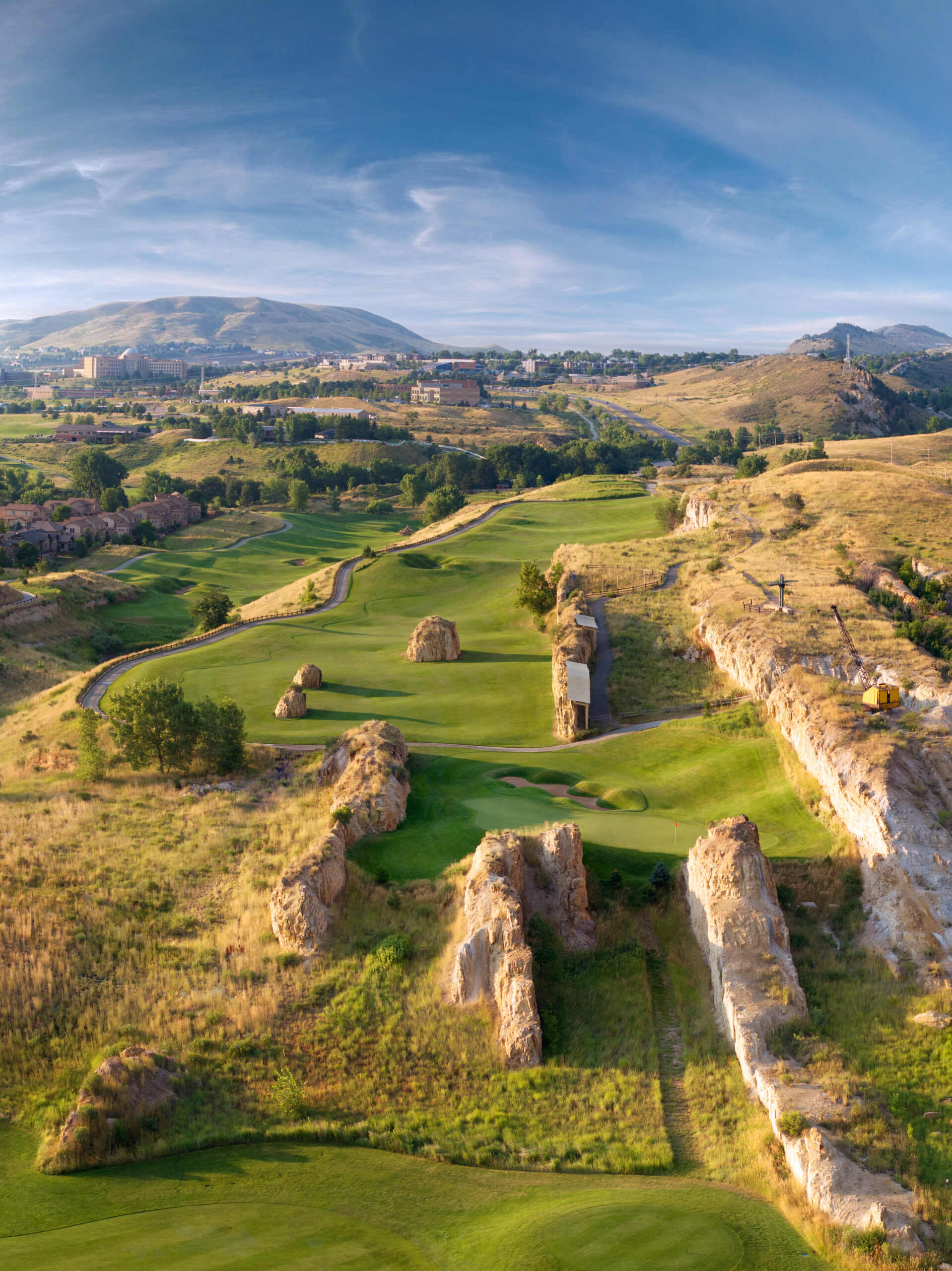 Breathtaking aerial view showcasing multiple golf holes winding through dramatic sandstone cliffs and desert terrain with city views in the distance.