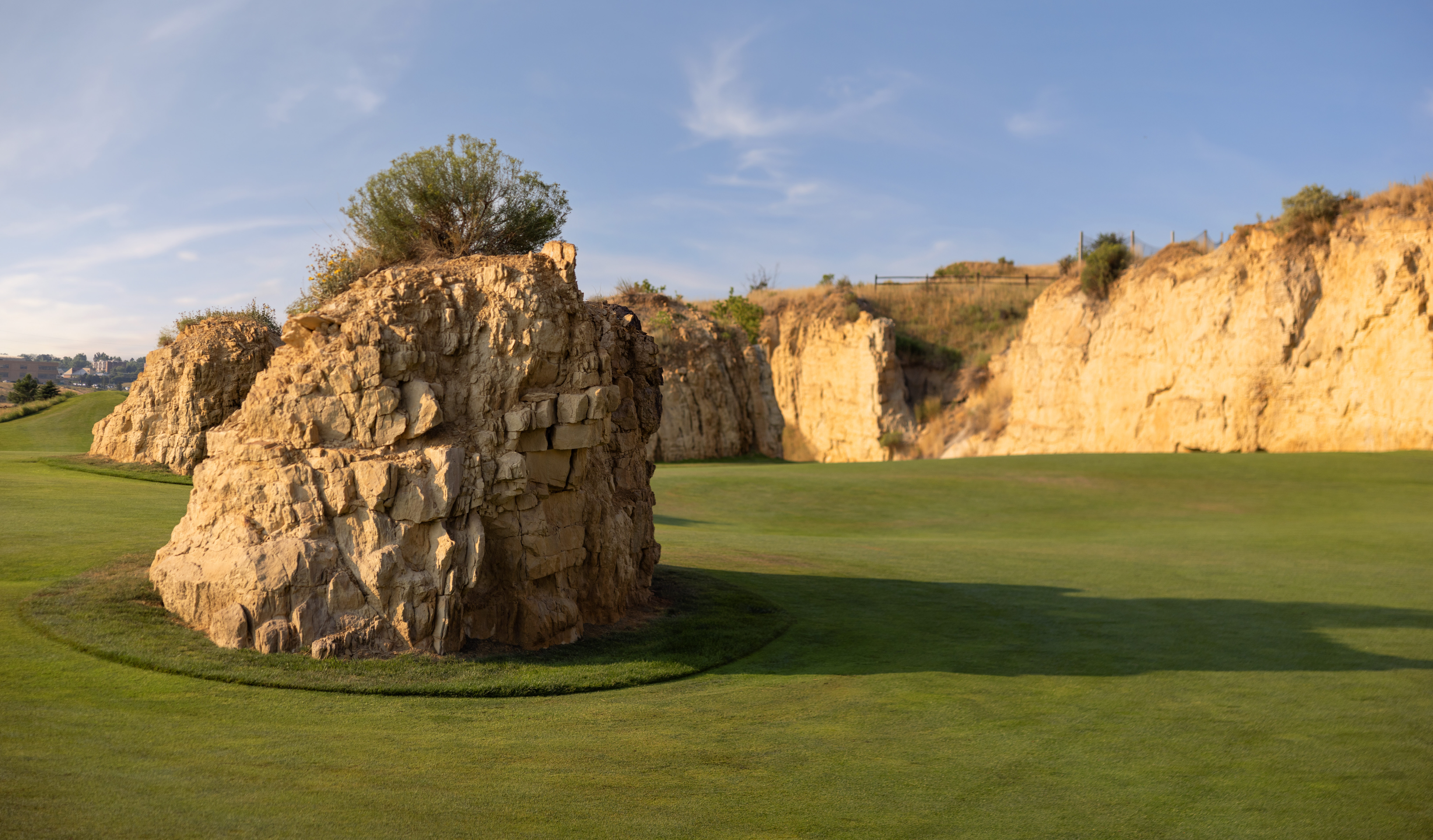 A dramatic golf hole featuring ancient stone ruins with a tree growing from the top, set against golden limestone cliffs and manicured fairways under warm lighting.