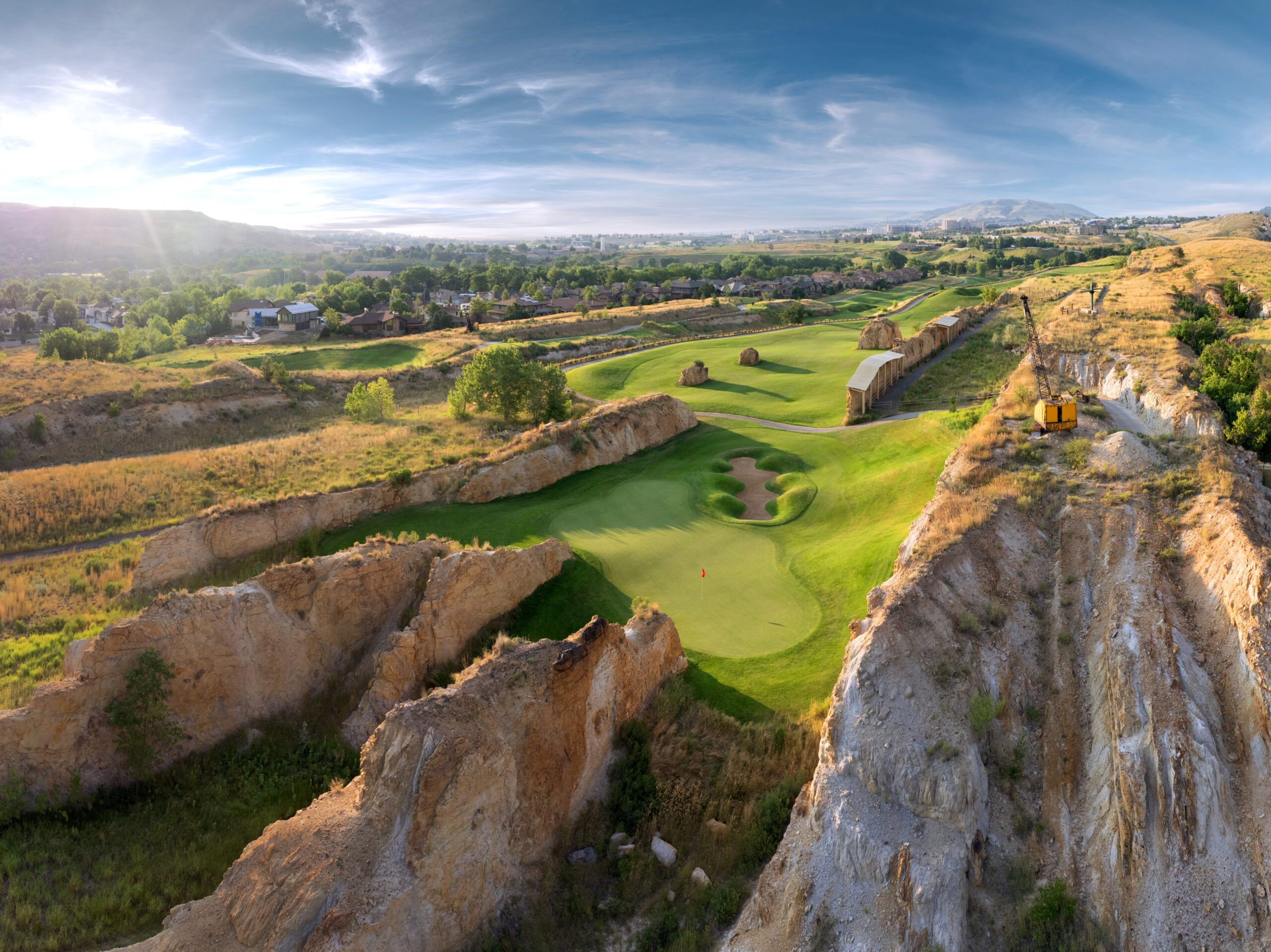 Stunning aerial view of golf holes carved through towering sandstone canyon walls with dramatic shadows and natural rock formations.
