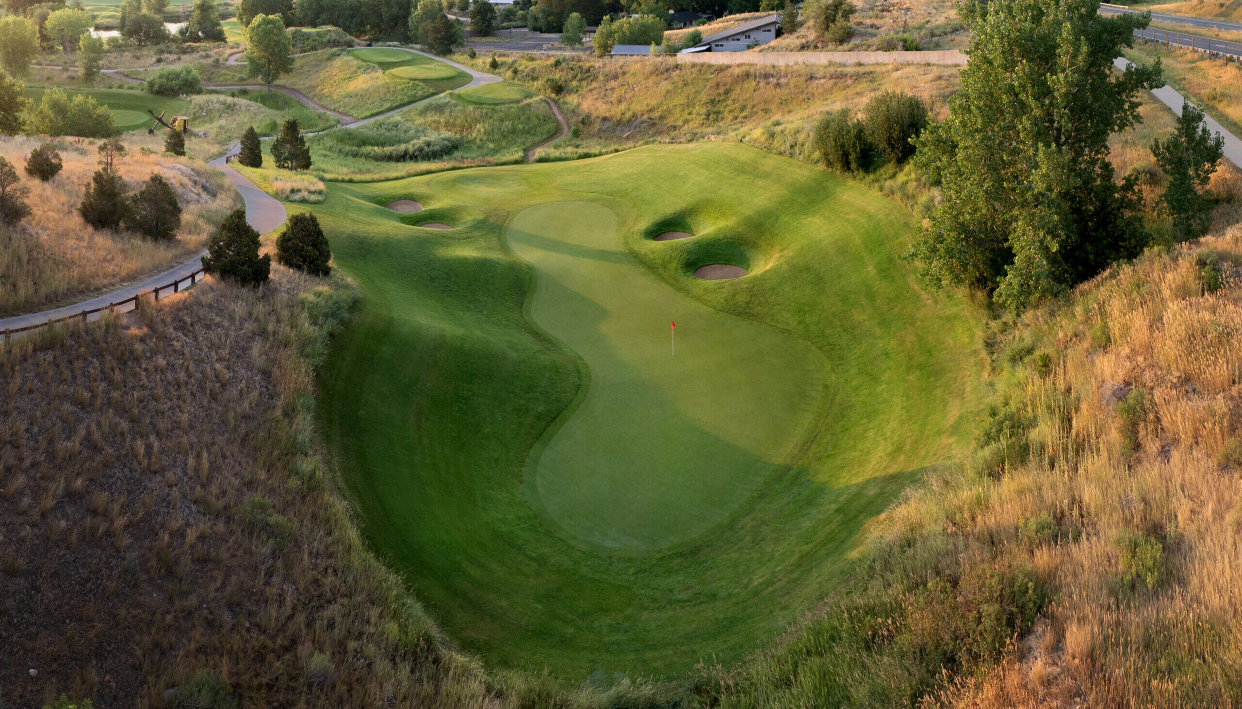 Aerial view of an undulating green complex with multiple sand bunkers surrounded by native desert vegetation and cart paths.