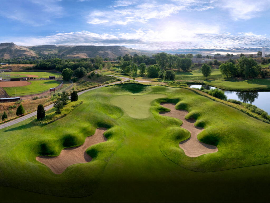 Aerial perspective of a challenging golf hole with multiple sand bunkers, water hazard, and mountain backdrop.