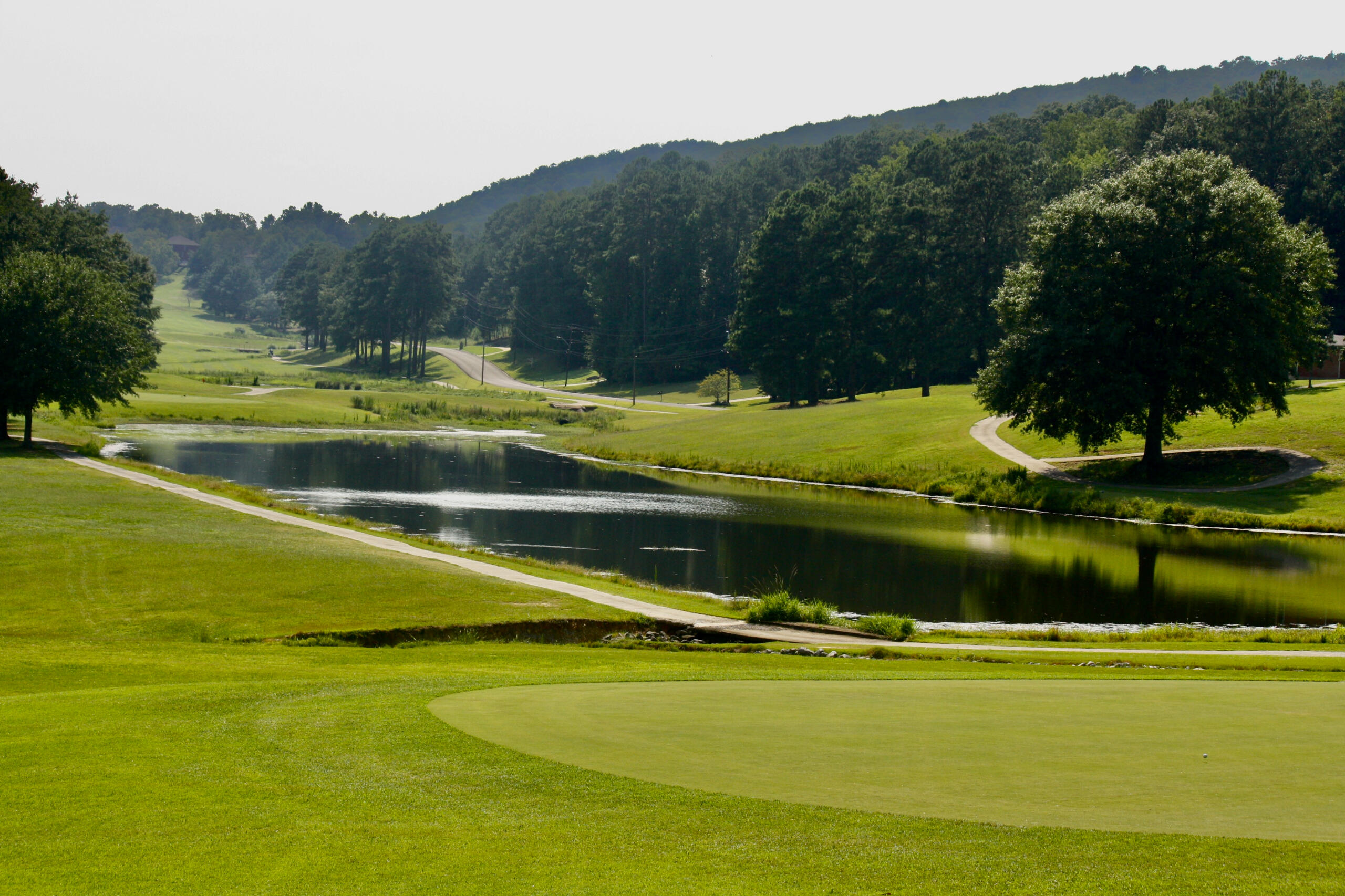 Breathtaking morning view from a green looking across a large water feature toward multiple fairways winding through the valley with forested hills in the misty background.