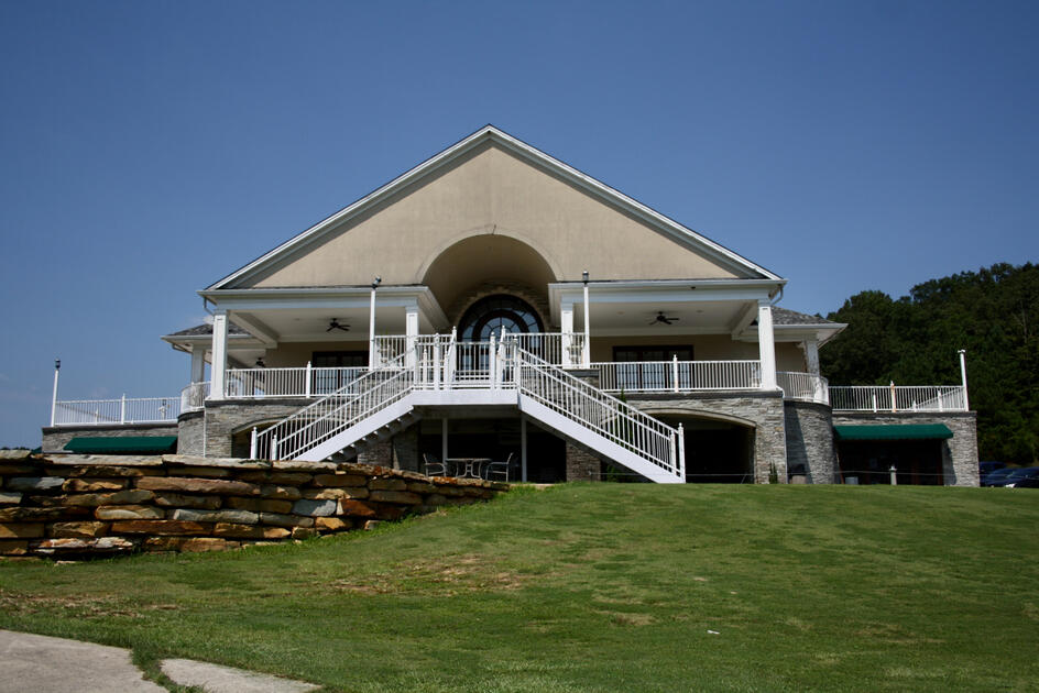 Two-story clubhouse building with white columns, covered porches, stone accents, and grand staircase leading to the main entrance.