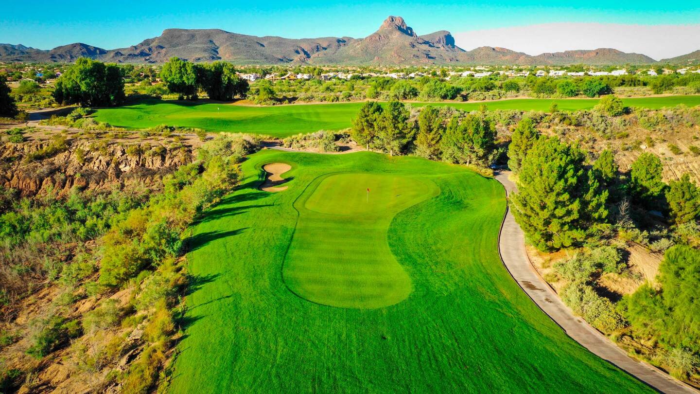 Stunning aerial view of Quarry Pines Golf Club showing pristine green fairways winding through desert terrain with dramatic mountains in the background and residential areas visible.