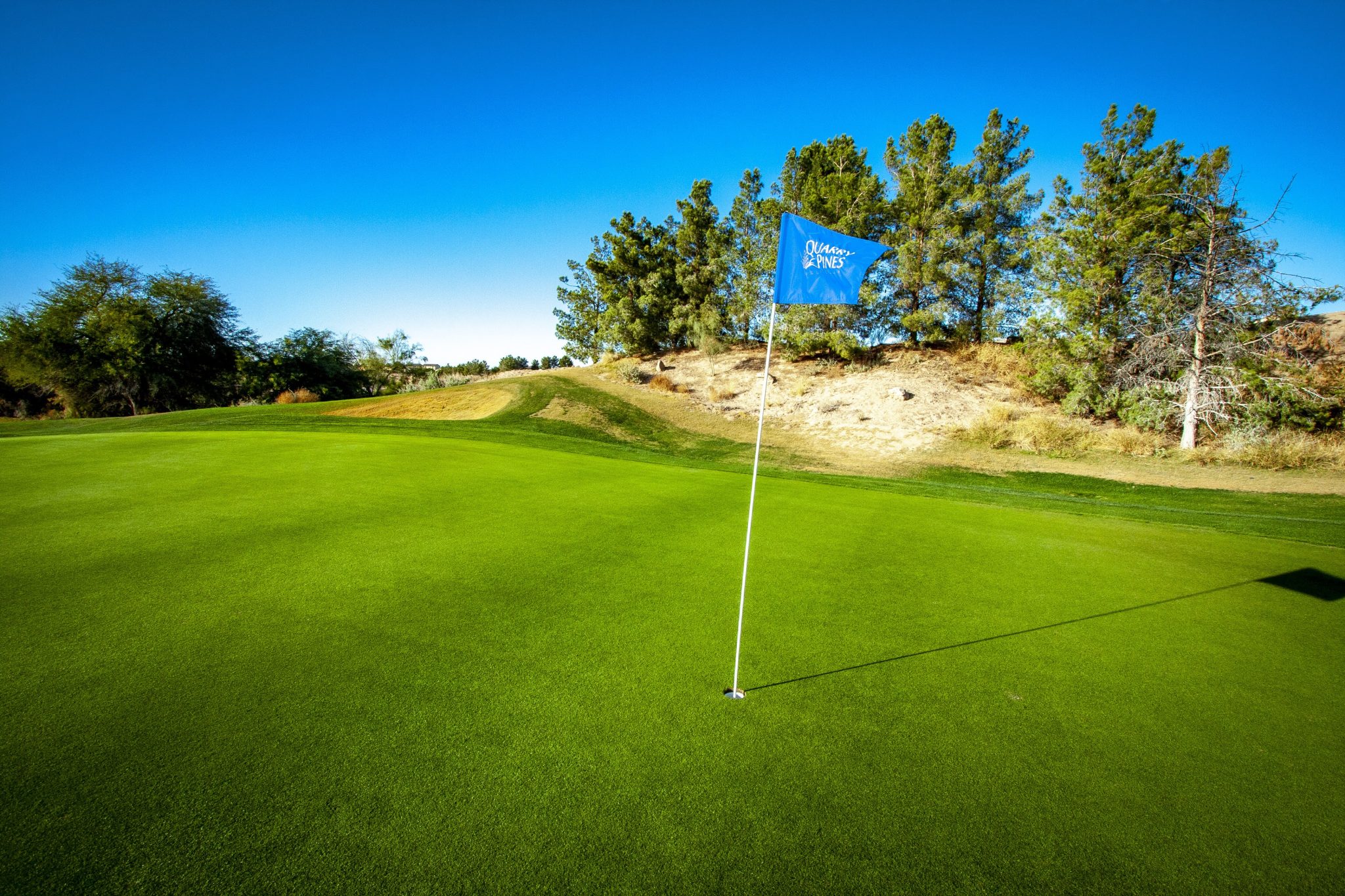 Dramatic tee box view looking down into a canyon with the green nestled between towering desert rock formations and mountain vistas in the distance.