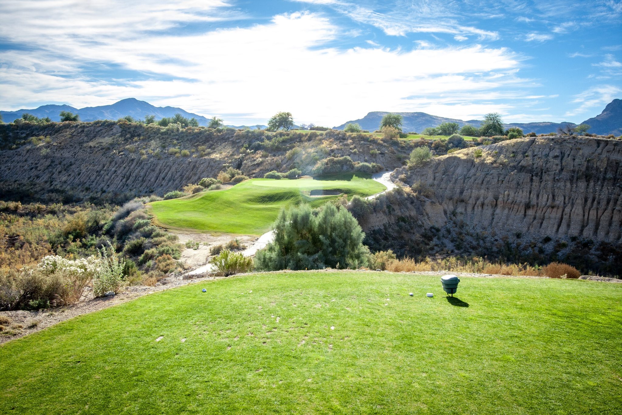 Aerial perspective of a challenging desert golf hole with an elevated green, multiple bunkers, and distinctive red rock formations creating natural hazards.