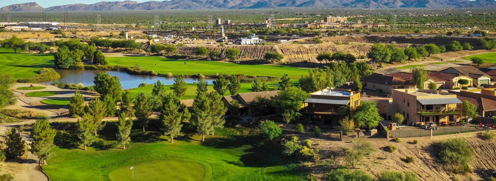 Panoramic view of Quarry Pines Golf Club showing the clubhouse complex, practice facilities, and course layout with mountains and desert landscape in the background.
