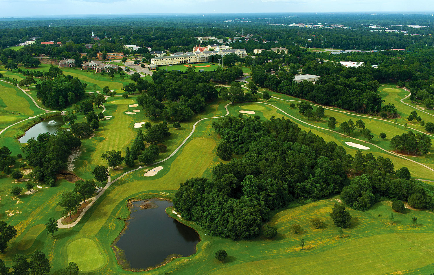 Stunning aerial view showcasing the entire Spring Hill College Golf Course layout with multiple holes, water hazards, and the college campus buildings in the background.