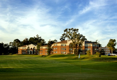 Modern clubhouse building with red brick architecture set against mature trees and well-maintained fairway in golden hour lighting.