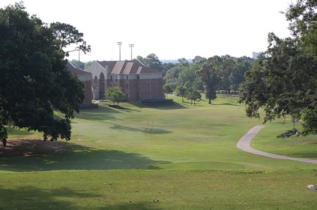 An elevated view of the golf course showing rolling fairways, a cart path, and a large clubhouse building nestled among dense trees.