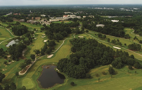 Aerial view of Spring Hill College Golf Course showing multiple holes, fairways, water features, and the surrounding forested landscape with campus buildings visible in the background.
