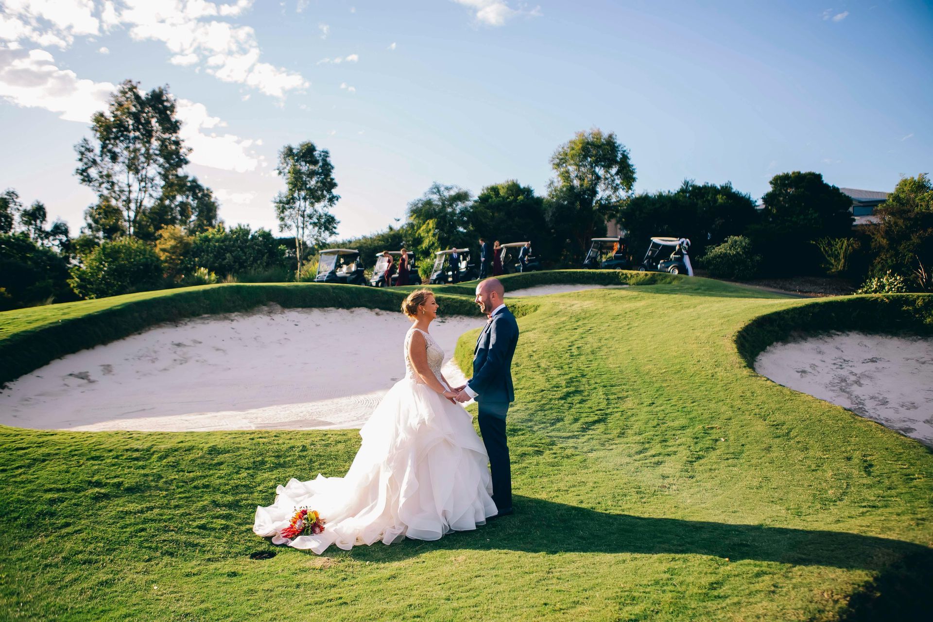 Bride and groom posing on the golf course green with sand bunkers and golf carts visible in the background, showcasing wedding venue capabilities.