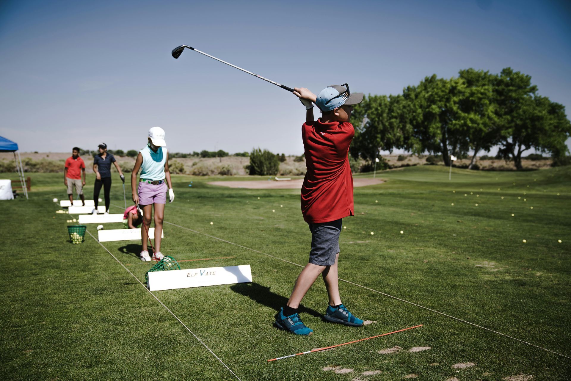 Young golfer practicing his swing at a driving range with organized practice stations and training aids.