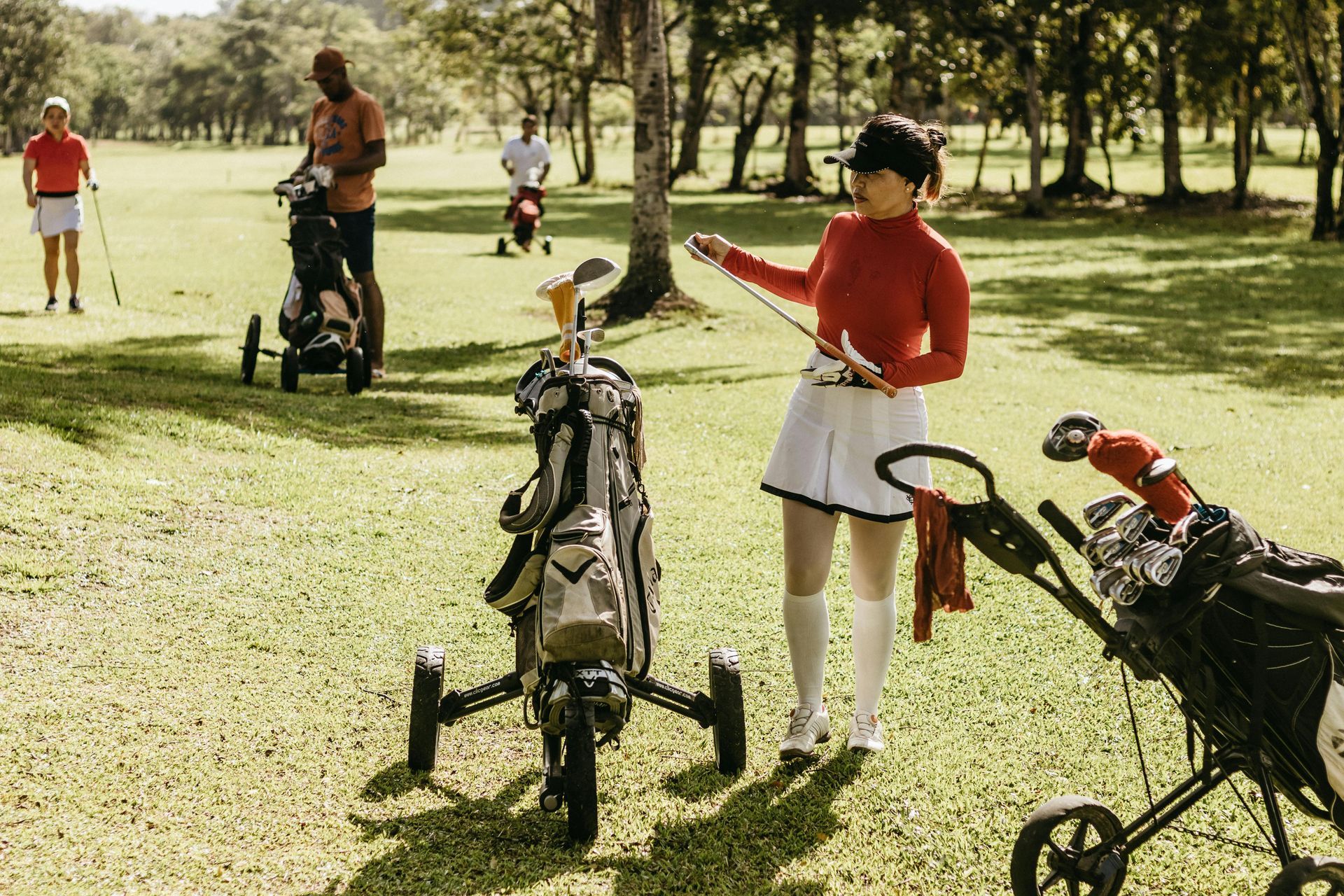 Female golfer in stylish attire checking her scorecard while standing with her pull cart on the golf course.