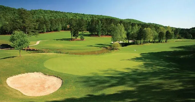 Panoramic aerial view of multiple fairways and greens with prominent sand bunker in foreground, showcasing the course layout against forested hills.