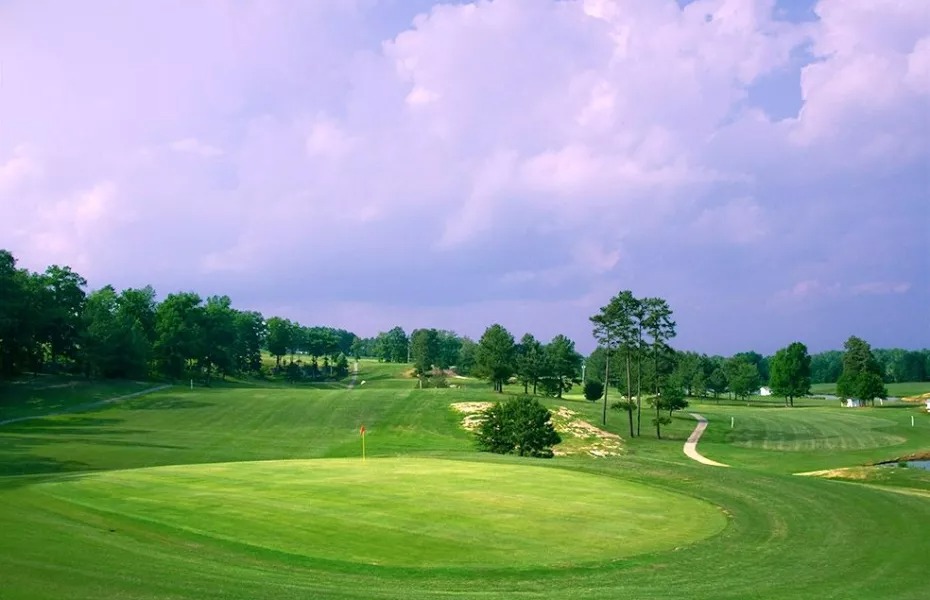 Well-maintained putting green with flag stick visible, surrounded by expertly manicured fairways and cart paths, showcasing the course's pristine playing conditions and professional upkeep.