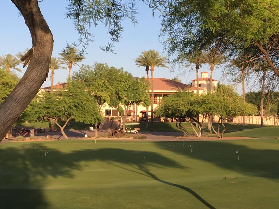 Legacy Golf Resort clubhouse viewed from the putting green during golden hour, showing the Mediterranean-style architecture with palm trees and desert landscaping.