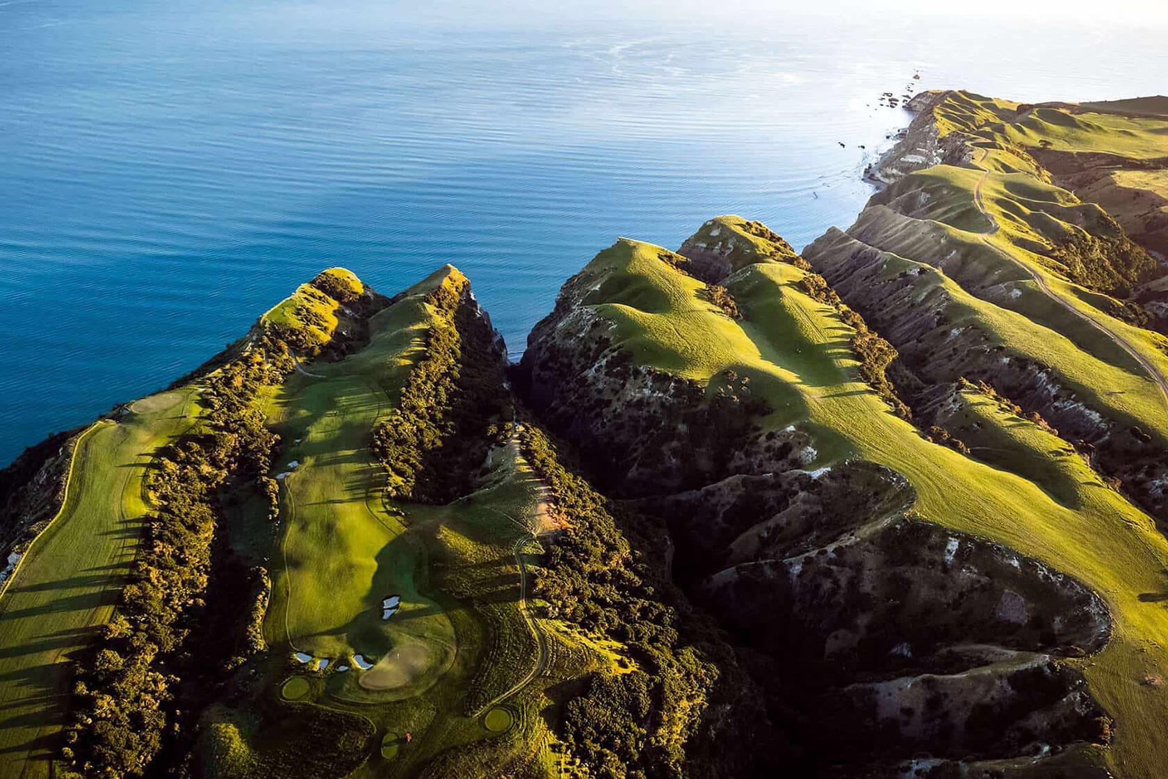 Breathtaking aerial view of dramatic coastal golf holes carved into clifftop terrain overlooking deep blue ocean waters.