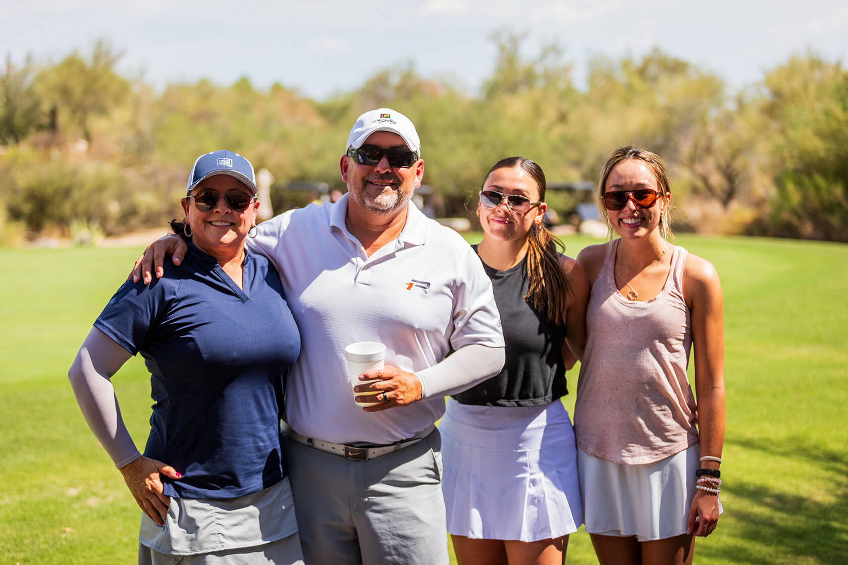 A group of four people in golf attire posing together on a golf course with desert mountain scenery in the background.