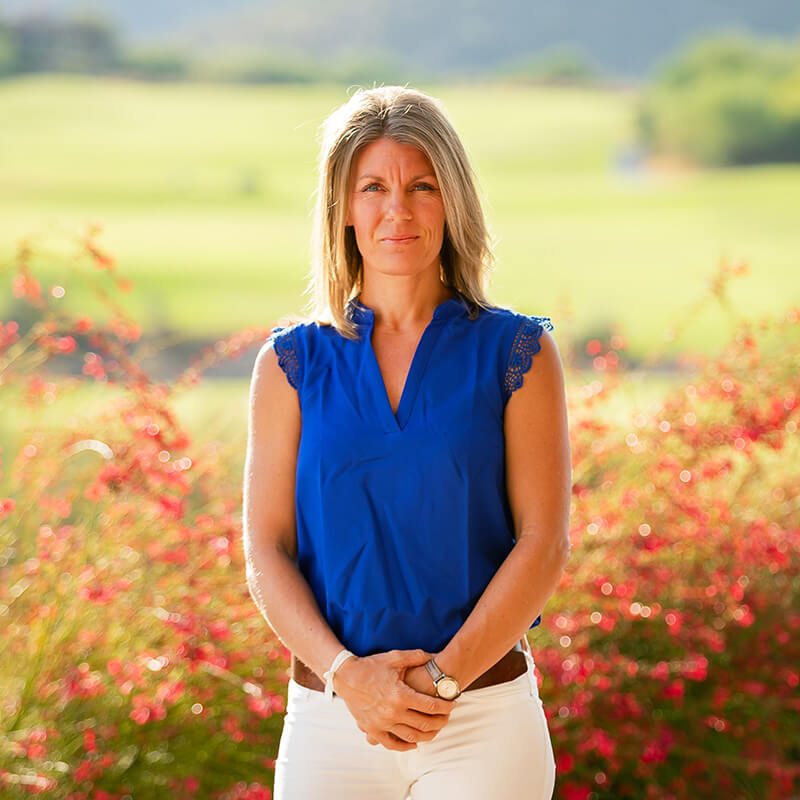 Professional headshot of Rebecca Shaughnessy, a club staff member, posed outdoors with beautiful soft lighting and colorful wildflower background.