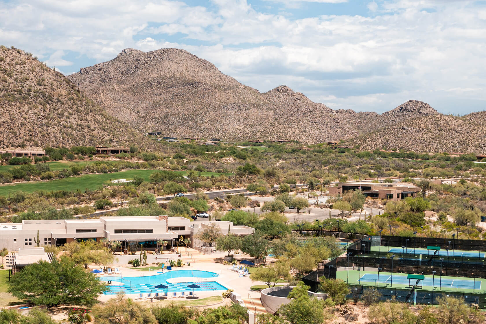 Modern desert-style clubhouse and amenities complex featuring swimming pool, tennis courts, and contemporary architecture set against Arizona mountain landscape.