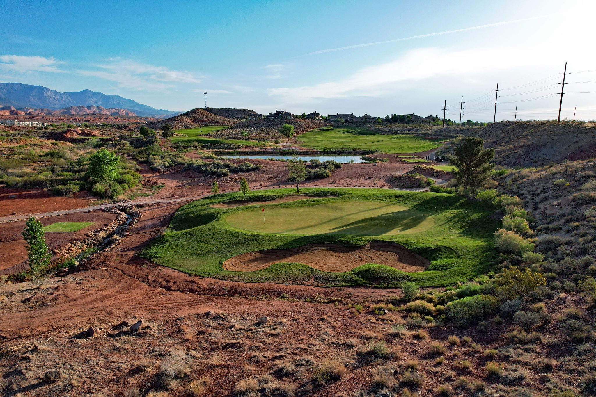 Stunning side view of the 3rd hole featuring an elevated green surrounded by red rock formations, water hazard, and desert mo