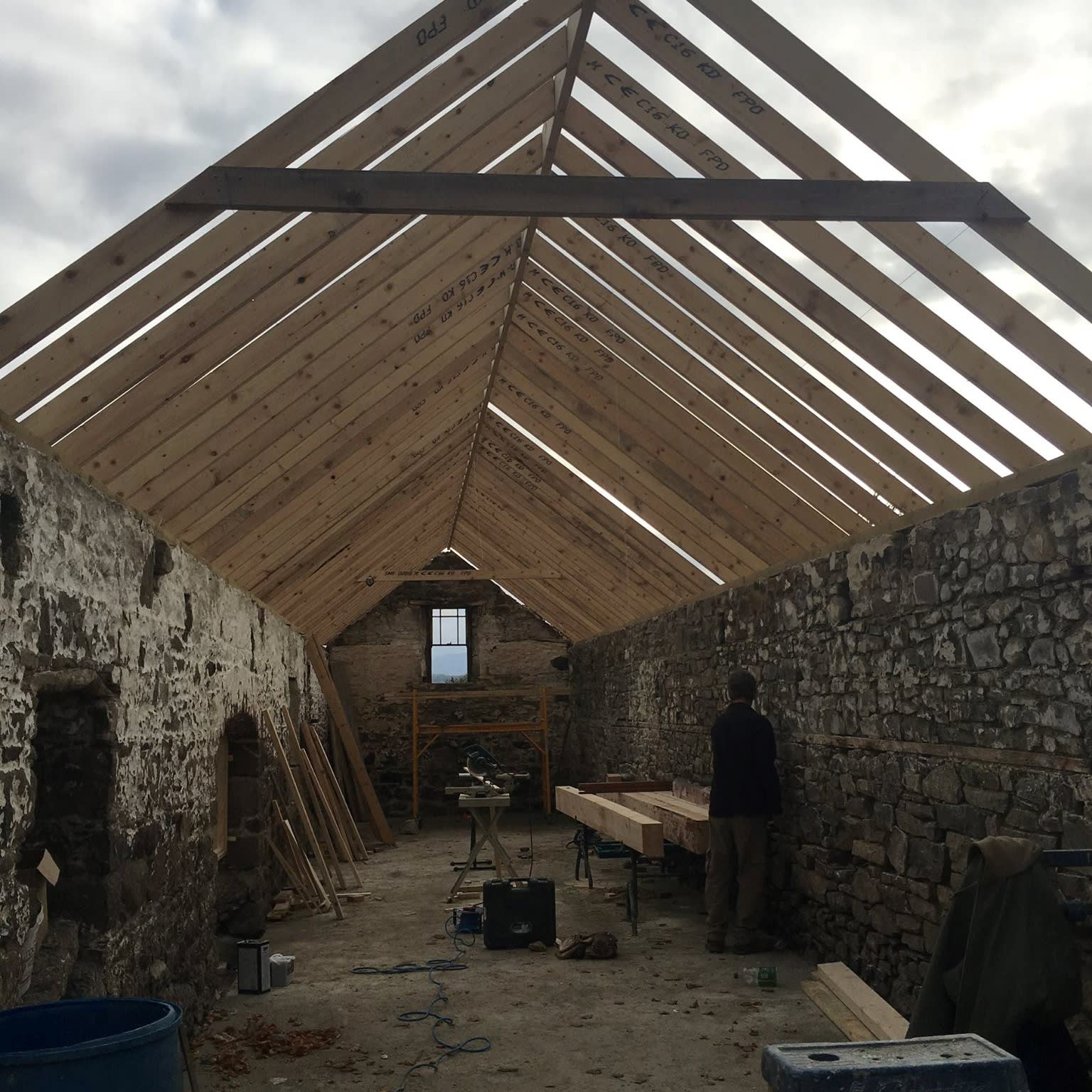 A roof being built onto the stone wall frame of an old barn house