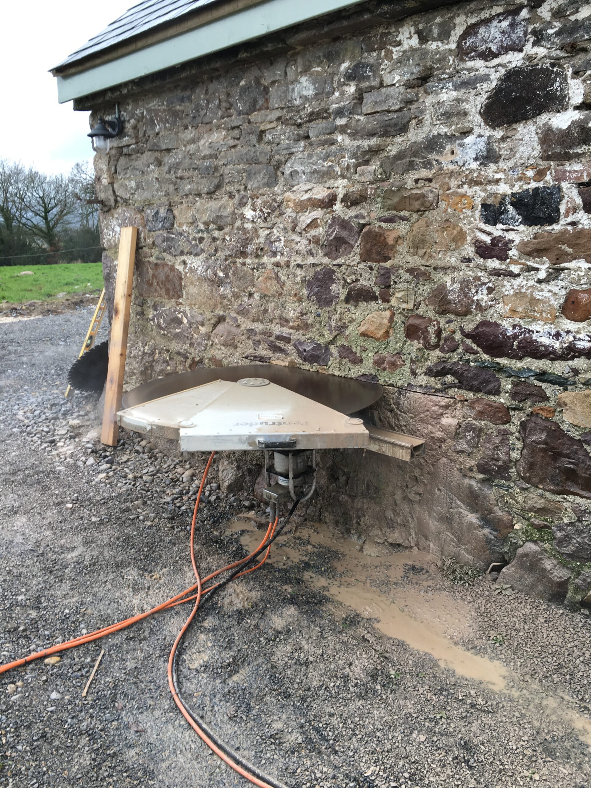 A circular saw being used to cut into the side of a stone barn.