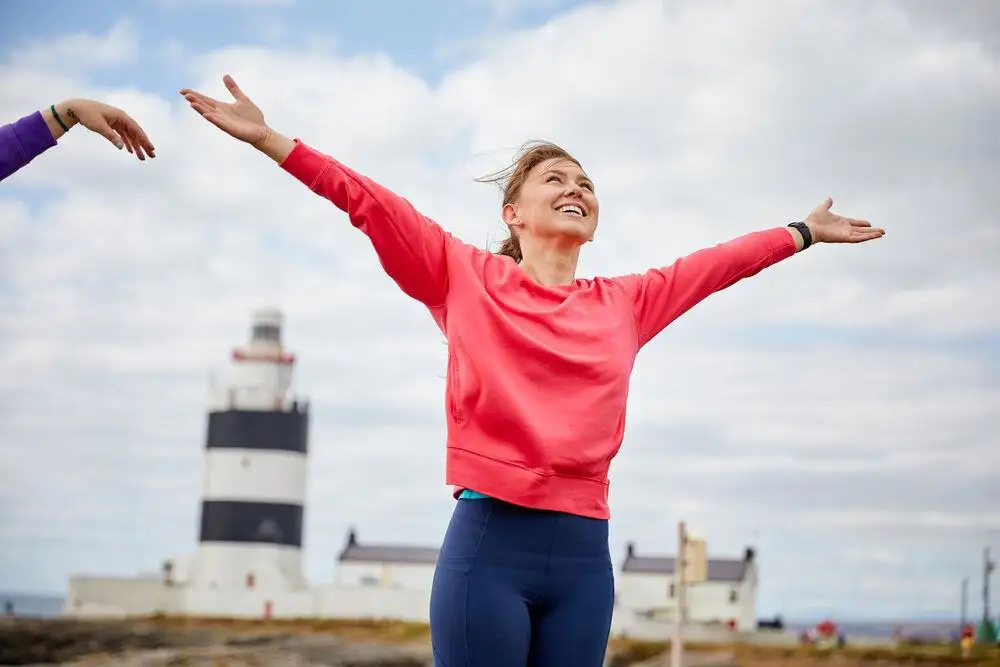 i_h9b46f3c73ce3be0b2eed6f846e688f8fc3a88ff2 woman posing with arms stretched out in front of hook lighthouse Wexford, Ireland