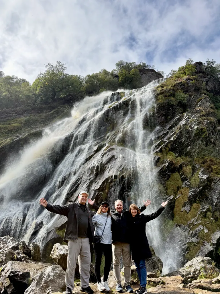 two couples on a tour of ireland posing below a waterfall.